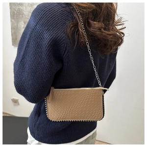 Detail of khaki faux-crocodile crossbody bag with silver studs and chain strap on a model