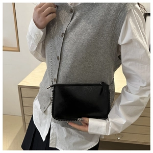 Detail of black crossbody bag with silver studs and metal chain strap on model
