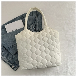 Close-up of white quilted puffer tote bag on white fabric with artistic book and denim