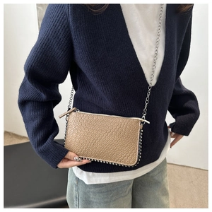 Detail of khaki crocodile pattern crossbody bag with silver rivets and metal chain strap