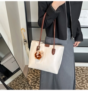Détail du sac fourre-tout en cuir ivoire avec des poignées brunes et un petit charm