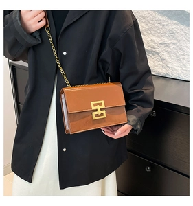 Detailed side view of a brown glossy leather crossbody bag with golden chain and square buckle