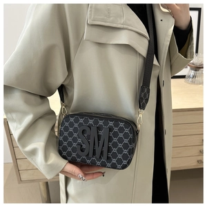 Close-up of grey textured camera bag featuring a black SM patch and woven wide strap