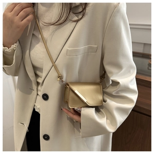 Dettaglio di una mini borsa a tracolla oro metallizzato abbinata a un blazer beige