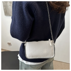 Silver crocodile texture crossbody bag with metal chain on a model in navy knitwear