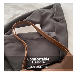 Close-up detail of dark brown leather handle on a minimalist underarm bag and grey suit