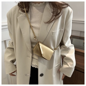 Dettaglio mini borsa a tracolla oro champagne con finitura opaca su un blazer beige