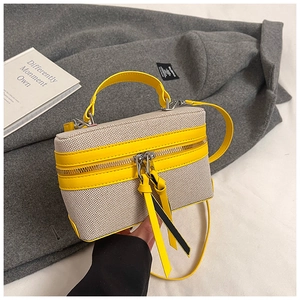 Detail of box-shaped canvas bag with bright yellow leather trim and silver metal hardware