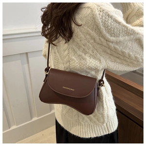 Detail view of a brown matte leather shoulder bag with gold lettering and a curved base