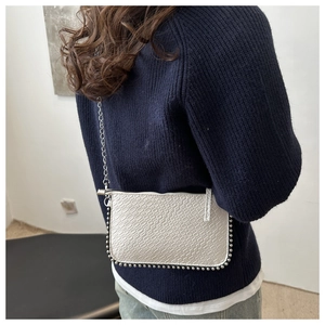 Detail of white crocodile embossed leather chain bag with silver studs on a female model