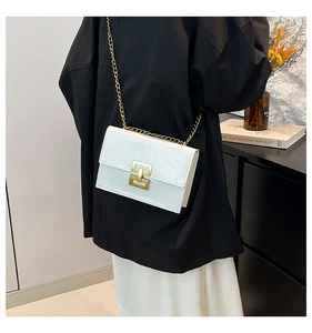 Detailed view of white textured leather small square bag with elegant gold chain strap