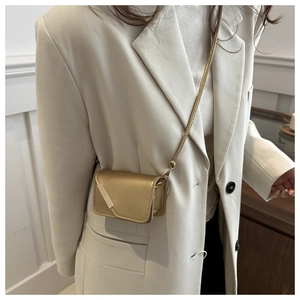 Dettaglio di una mini borsa a tracolla oro champagne metallizzato su un blazer crema
