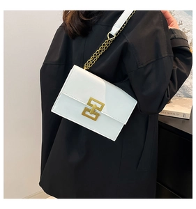 Close-up of white leather crossbody bag with gold chain strap and geometric metal buckle