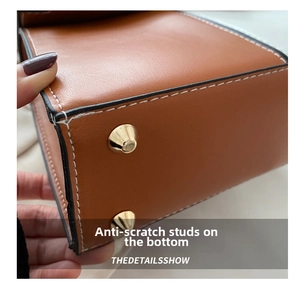 Détail du fond d'un sac en cuir marron avec surpiqûres blanches et clous de protection