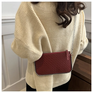 Detail of red woven crossbody bag with silver bead trim and metallic chain strap