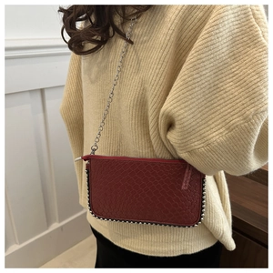 Detail of burgundy woven crossbody bag with silver rivets and metal chain on a beige sweater