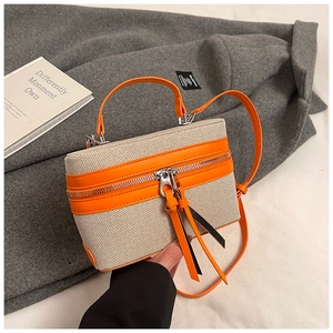Detail view of canvas crossbody bag with orange leather trim and long fringe zipper pull