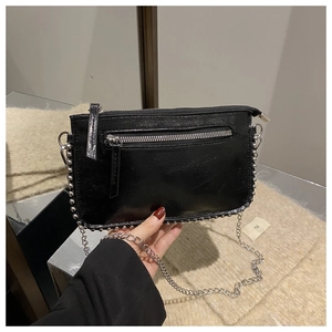 Detail of black glossy handbag with silver studs and chain strap held by hand