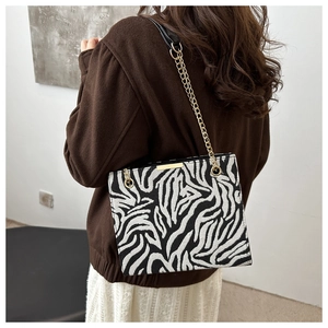 Détail du sac à bandoulière motif zèbre avec chaîne dorée porté par un mannequin femme
