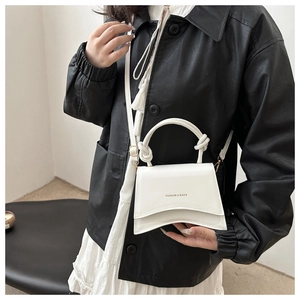 White handbag with a unique knotted circular handle and curved base shown on model