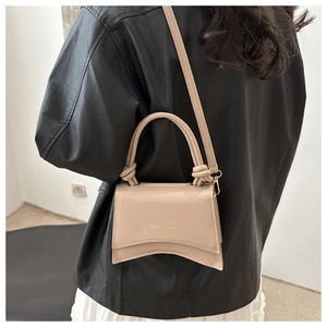 Close-up of beige leather mini bag with knot handle and curved base on black jacket