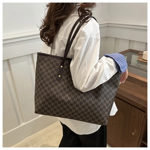 Detail of dark brown tote bag featuring all-over M pattern and gold rivet shoulder strap