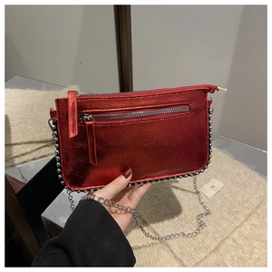 Detail of red metallic crossbody bag with silver studs and chain strap held by model