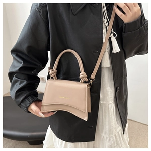 Detail of minimalist beige handbag with knotted handles and gold fashion lettering