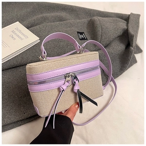 Detail of boxy beige canvas and purple leather bag with silver hardware on a grey coat