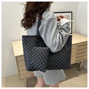 Close-up of a black tote bag with gray M-pattern print shown on model in a home setting