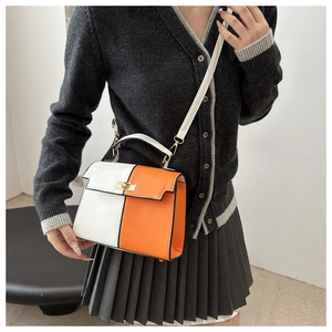 Detail view of contrast white and orange handbag with gold metal lock and shoulder strap