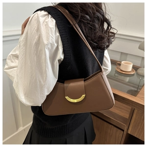 Close-up of brown crescent leather underarm bag with gold metal buckle on a model
