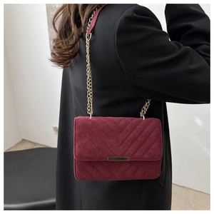 Detail of burgundy velvet crossbody bag showing V-quilted texture and gold chain strap