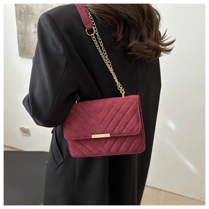 Detail of burgundy V-quilted suede bag with gold metal chain strap on shoulder