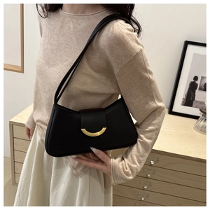 Chic black baguette bag with gold crescent buckle styled on a shoulder with beige knitwear