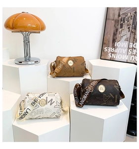 Detail view of printed barrel bags with letter motifs and gold circular emblems on a display
