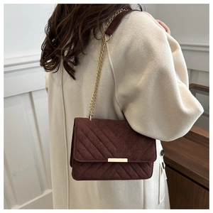 Detail of burgundy quilted suede shoulder bag with gold chain strap on cream coat
