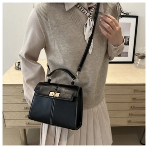 Detail of black faux leather Kelly bag with gold twist lock and white contrast stitching