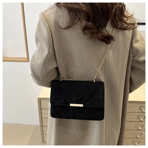 Detailed view of black quilted flap bag with gold chain strap on model for size reference