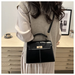 Detail of a black leather handbag with white stitching and a golden metal clasp