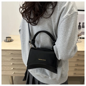 Detail view of a minimalist black square bag with gold lettering and slim shoulder strap