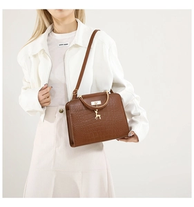 Detail of brown crocodile pattern handbag with golden metal handle and deer charm