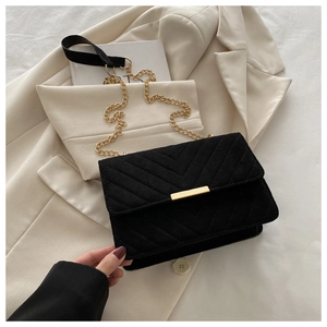 Detail of black quilted suede shoulder bag with gold chain strap on beige blazer