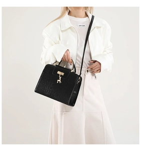 Detail of black crocodile pattern handbag with gold deer charm and round metal handle