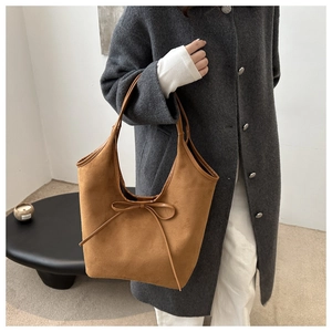 Detail of a brown suede tote bag featuring a decorative bow drawstring and soft texture