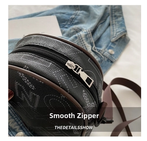 Detail showing smooth silver metal zipper and brown leather trim on a circular crossbody bag
