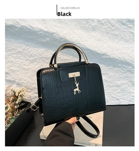 Detail of black crocodile embossed handbag with gold deer charm and round metal handle