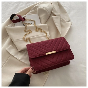 Macro detail of burgundy velvet crossbody bag with V-shaped quilting and gold metal buckle