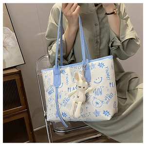 Close-up of white PU tote bag with blue cartoon graffiti prints and plush rabbit charm