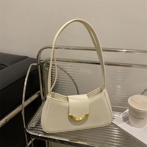 Chic cream leather underarm shoulder bag with a gold crescent buckle on a modern shelf